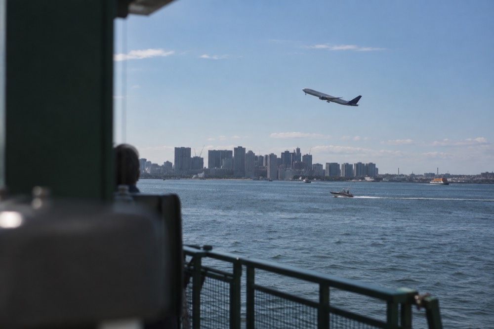 An airliner climbing away from Boston Logan Airport with harbor water below