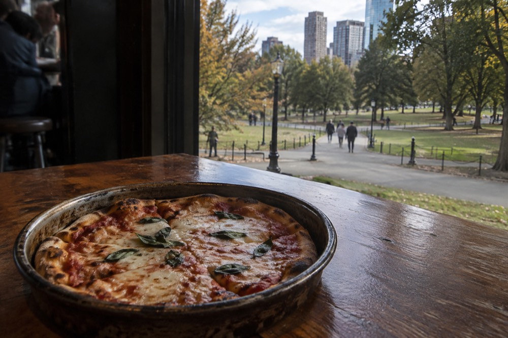 A small round thin-crust pizza in a well-worn metal pan sitting on a wooden bar top