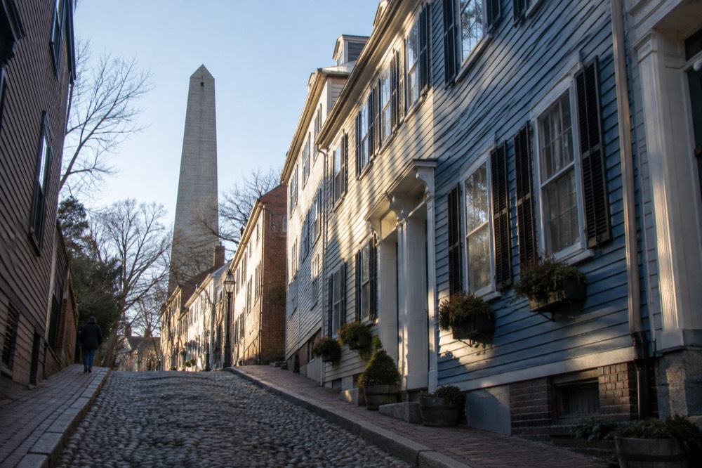 Rowhouses on a Charlestown hillside with the Bunker Hill Monument rising above the rooftops
