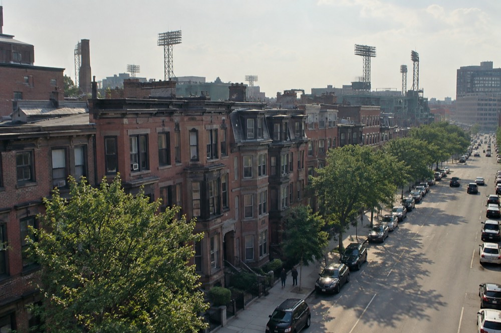 Brownstone buildings near Fenway Park with the ballpark's light towers rising behind them