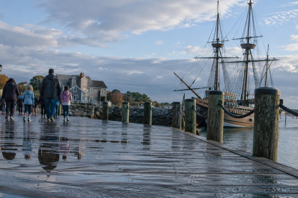 Families walking along a historic waterfront with a tall ship moored nearby