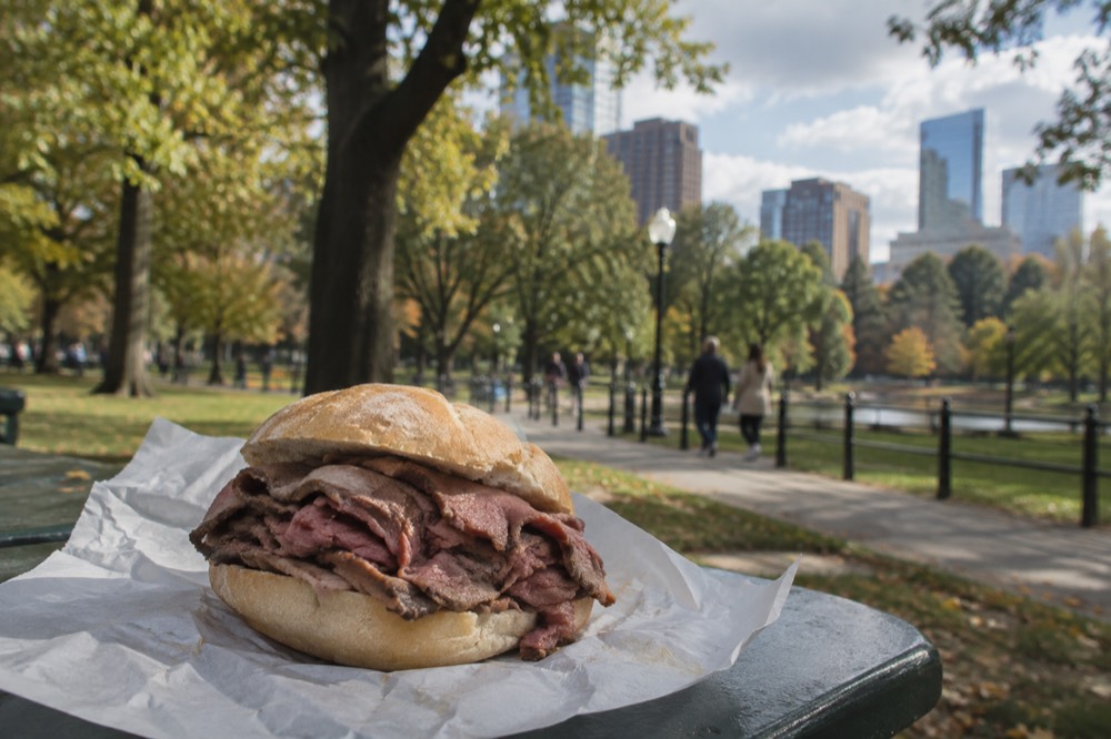 A roast beef sandwich piled with thin-sliced beef on a round roll on a deli counter