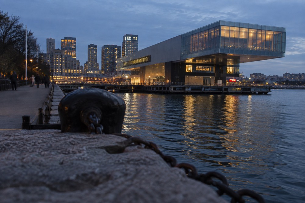 Cantilevered museum building extending over Boston Harbor at dusk with city lights reflecting on the water