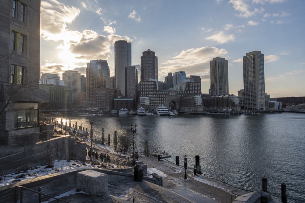 Boston harbor skyline under a partly cloudy sky, with water and downtown buildings visible