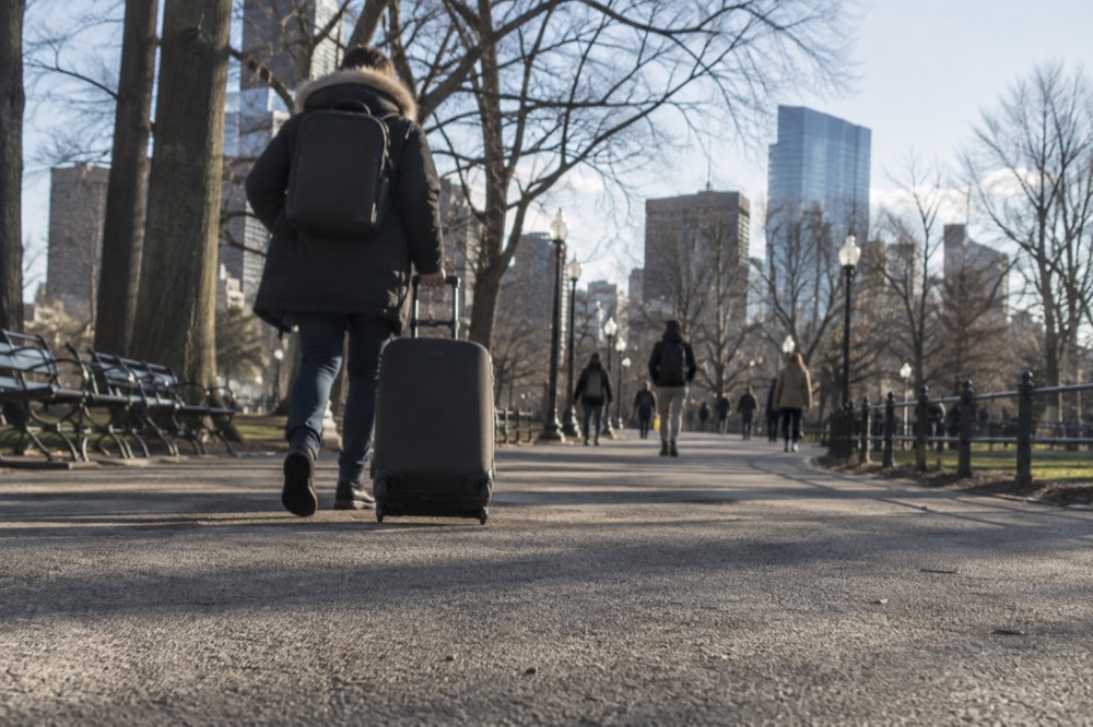 A traveler with a suitcase walking through a bright rail station concourse toward the platforms