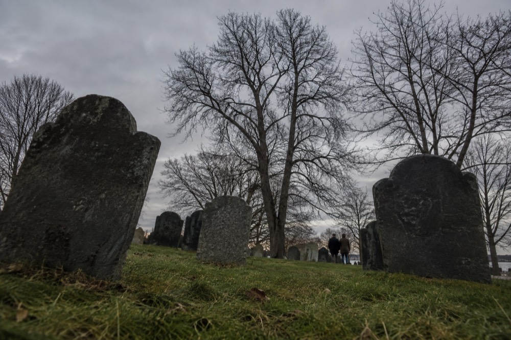 A weathered colonial burying ground with tilted slate slabs, grass, and bare trees