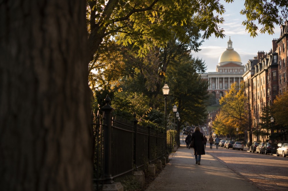 A red-brick historic Boston street with the gold-domed Massachusetts State House visible at the top