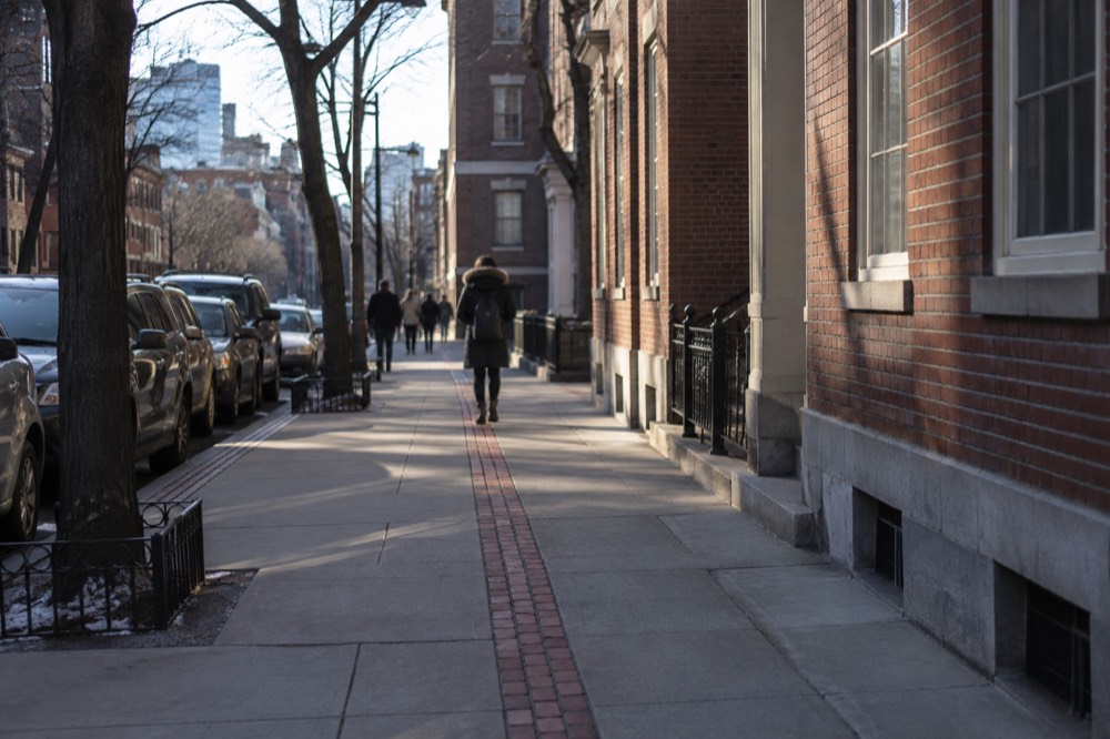 A red brick line marking the Freedom Trail running along a Boston sidewalk past historic buildings