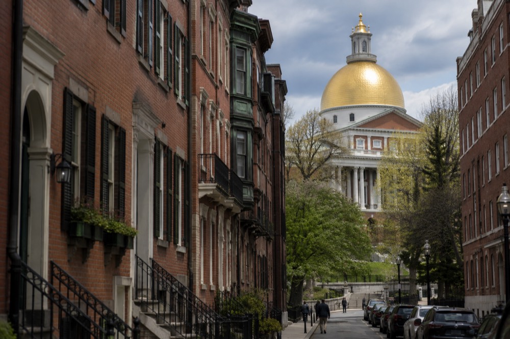 Red brick colonial buildings along a narrow Boston street with the gold dome of the Massachusetts State House rising behind them