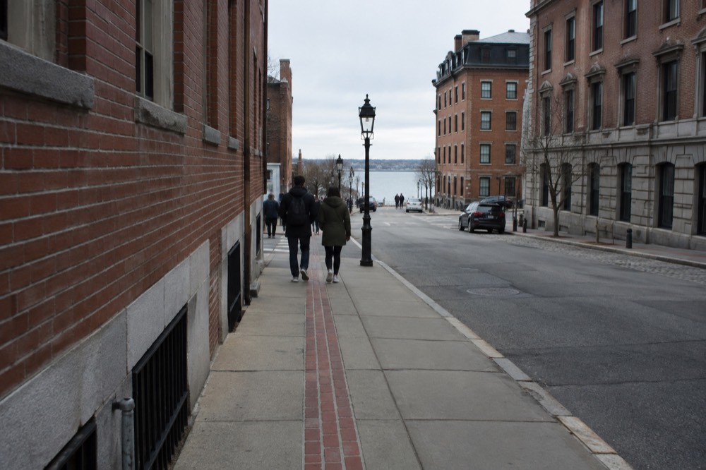 Visitors walking a red-brick freedom trail line past historic Boston buildings