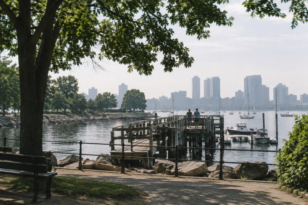 A wooden fishing pier over calm harbor water with small boats moored nearby