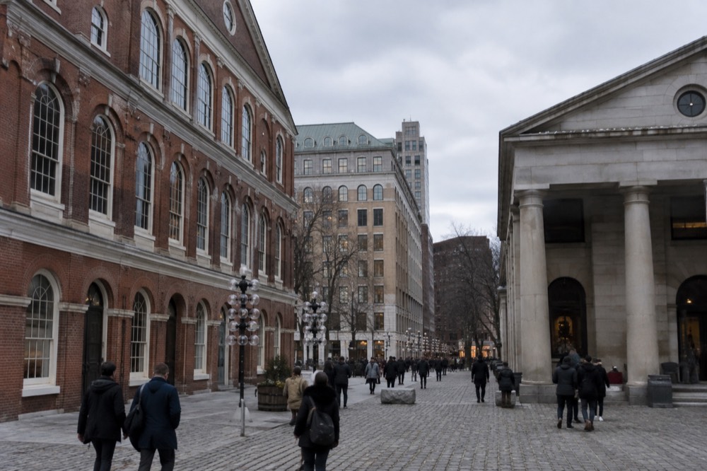 The red brick facades and granite columns of Quincy Market's market hall seen from the cobblestone promenade