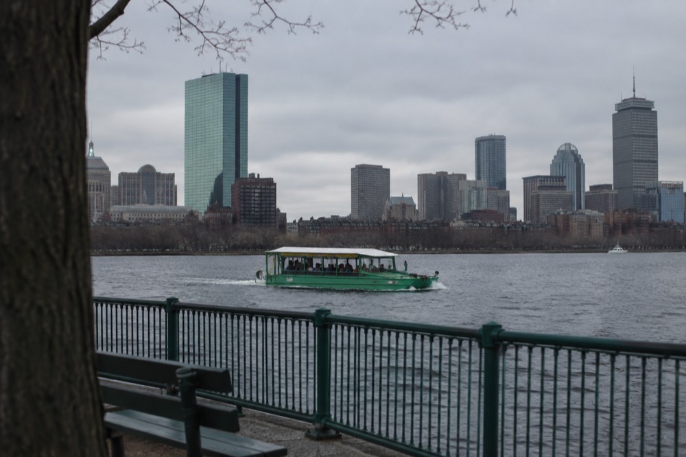 An amphibious duck boat cruising on the Charles River with the Boston skyline behind it