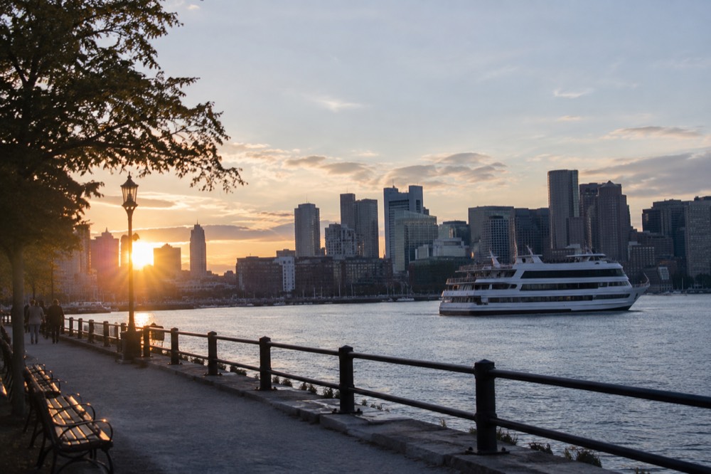 Boston's waterfront at dusk with a cruise boat and the city skyline behind it