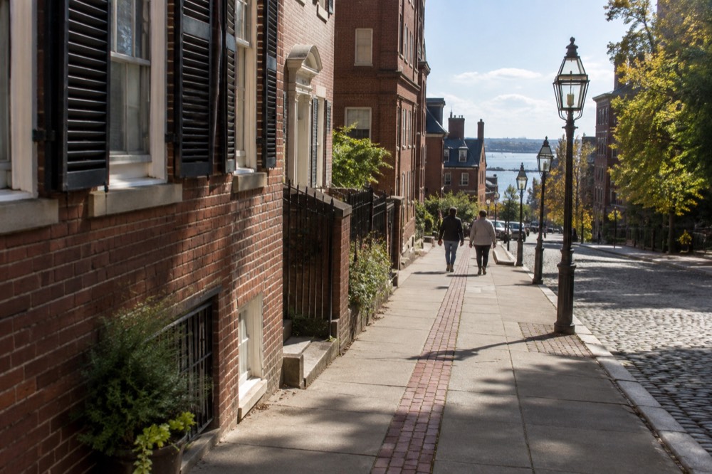 The red brick Freedom Trail line running along a Boston sidewalk toward historic buildings