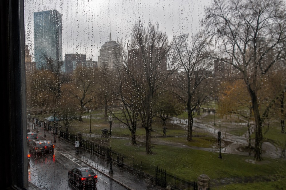 Raindrops on a window overlooking a Boston street with brick buildings and wet pavement