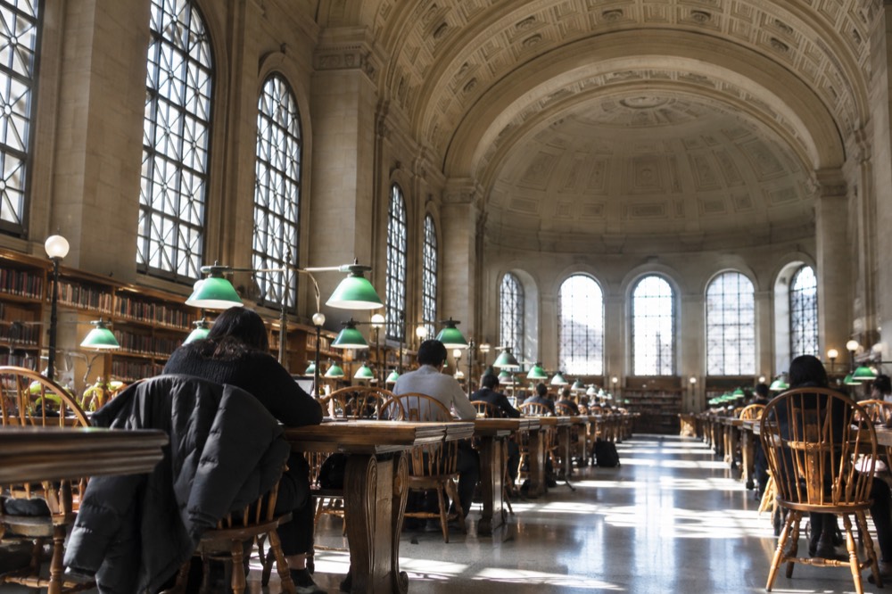 Readers seated at long wooden tables in the Bates Hall reading room of the Boston Public Library