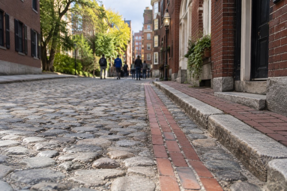 A red brick Freedom Trail line running along a cobblestone street past a colonial-era Boston building