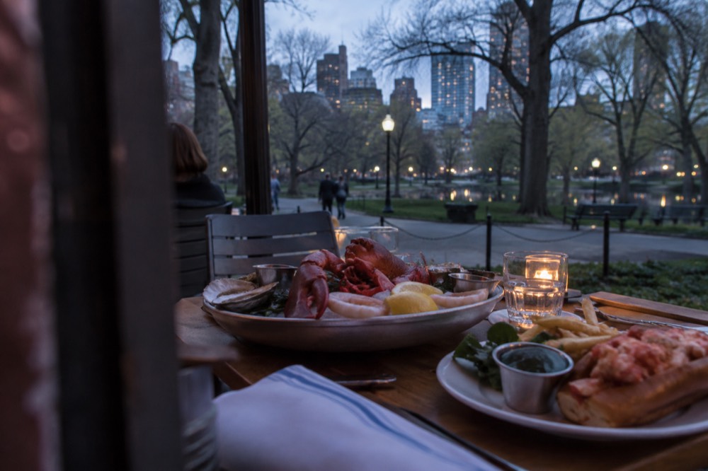 A platter of fresh seafood and a lobster roll on a wooden table at a Boston restaurant