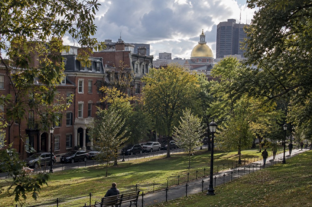 Red brick rowhouses on a tree-lined Boston street with the gold-domed State House visible behind them