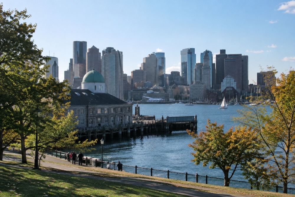 A view across Boston Harbor toward the city skyline, with a historic waterfront building in the foreground