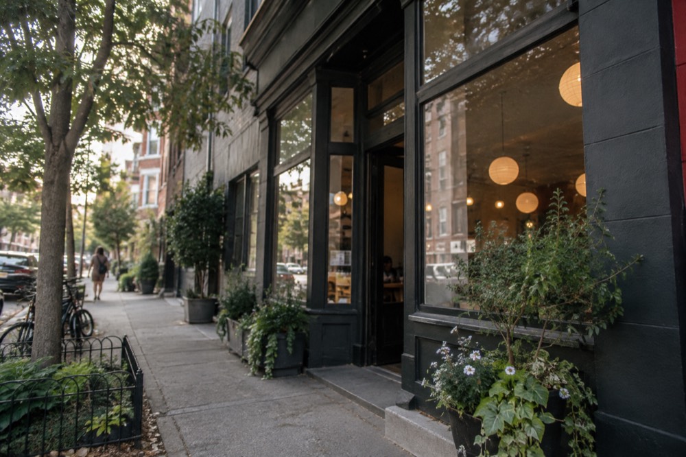 A small independent restaurant storefront with a lit sign at dusk