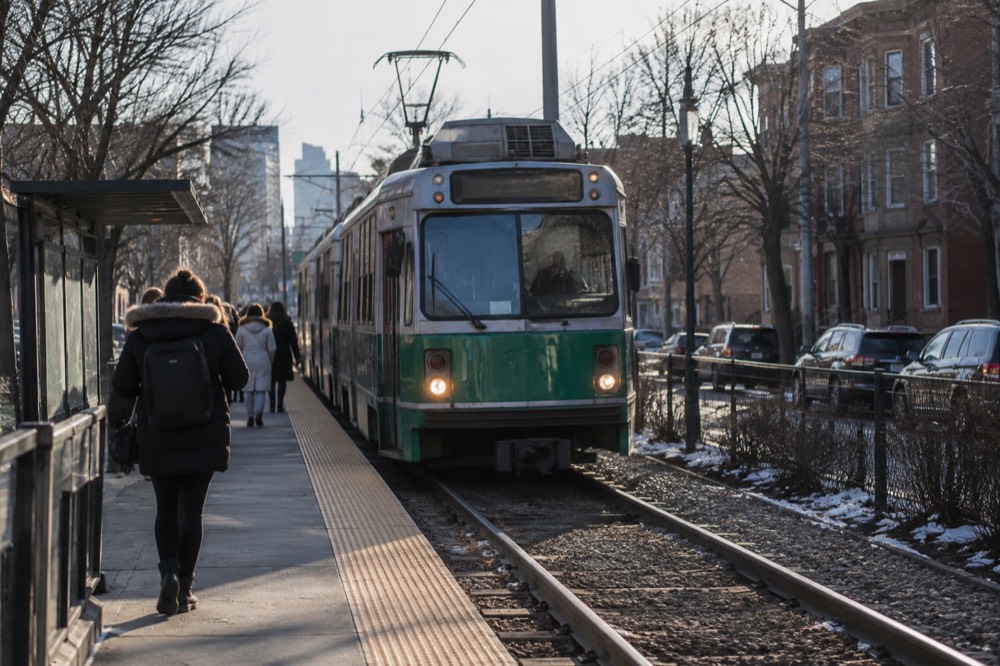 A Green Line trolley arriving at an above-ground stop beside a residential street