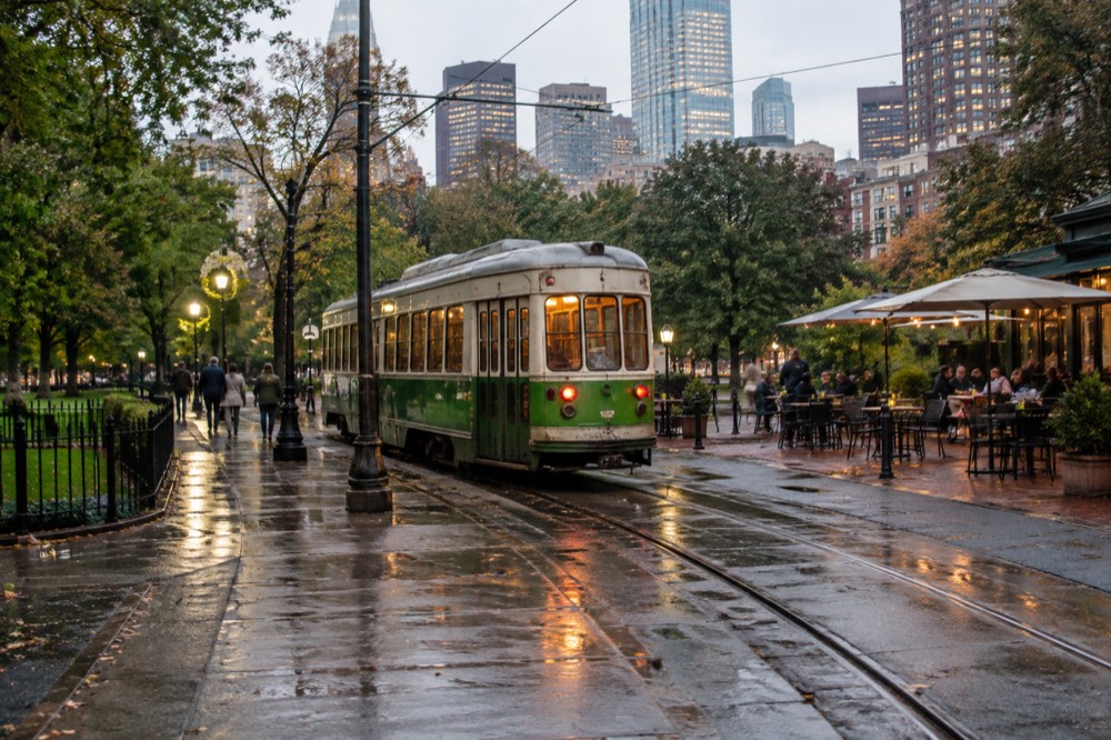 A small square with restaurants and outdoor seating around a trolley stop at dusk