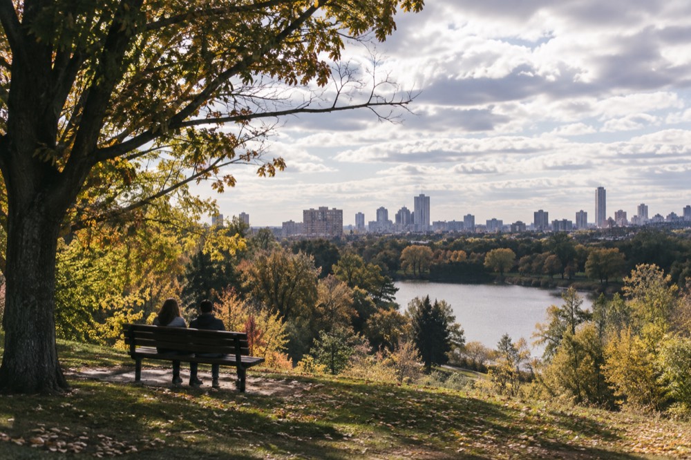 A hilltop park overlook with a pond below and a city skyline in the distance