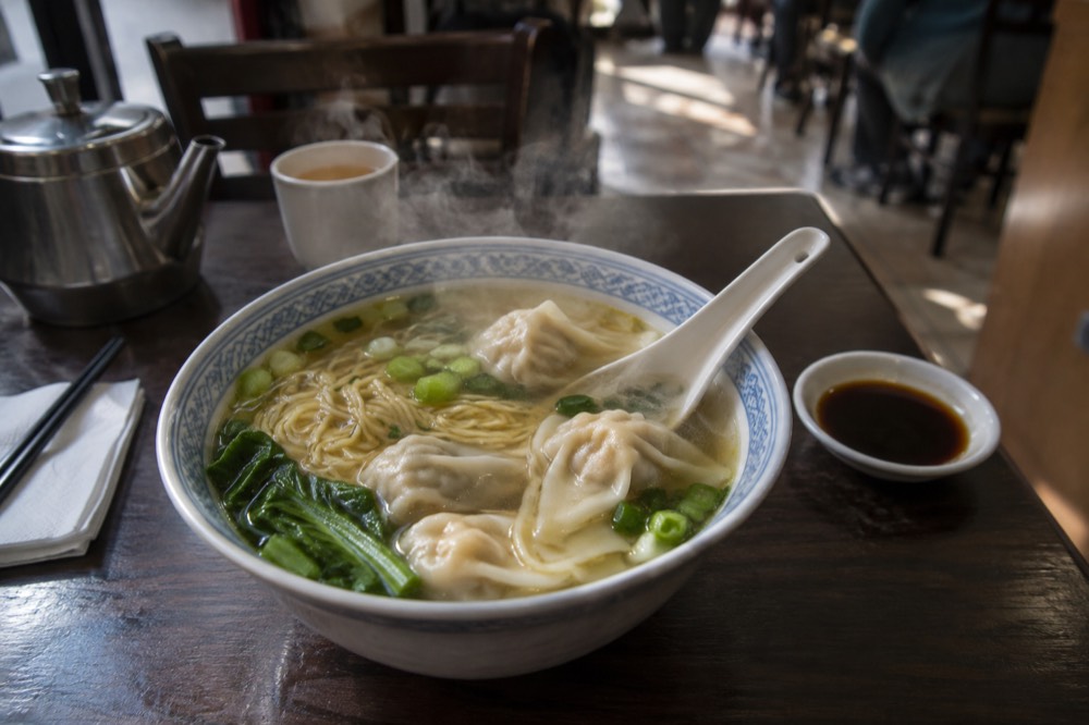 A steaming bowl of noodles and dumplings on a restaurant table