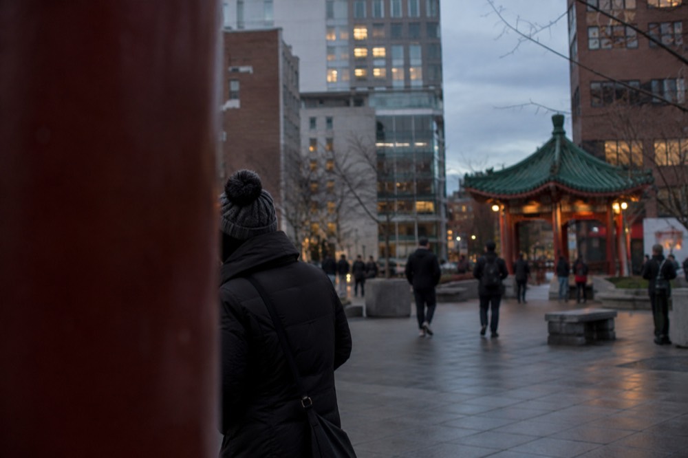 A Chinatown plaza at dusk with lit signs and a crowd gathered around a performance