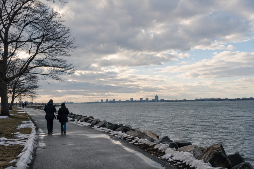A waterfront path in winter with bare trees and gray water beyond