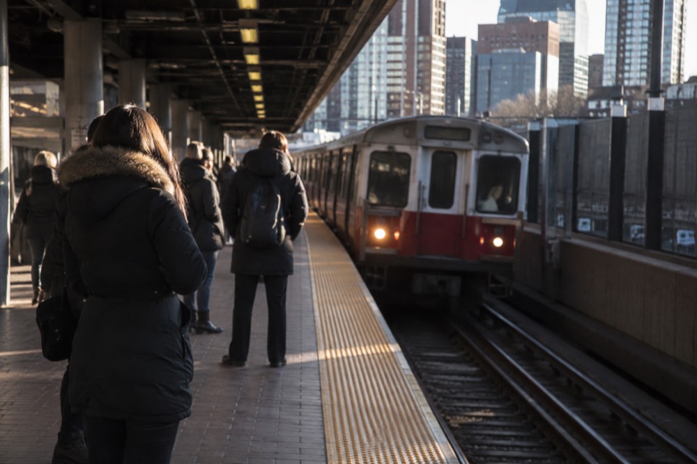 A subway platform with a red line train arriving and passengers waiting