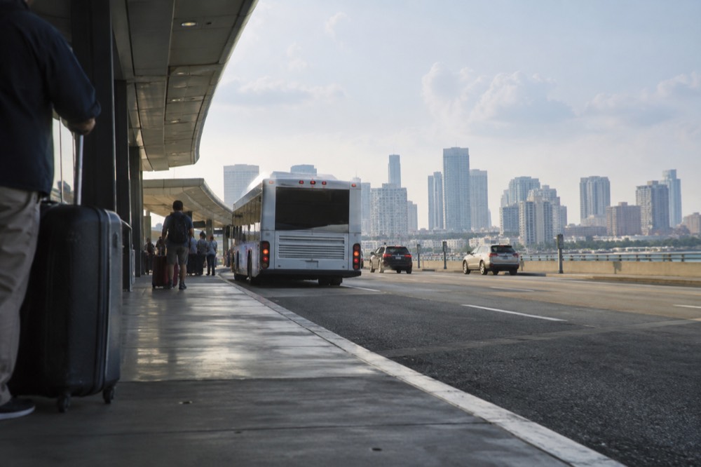 An airport terminal curb with a bus loading zone and skyline in the distance