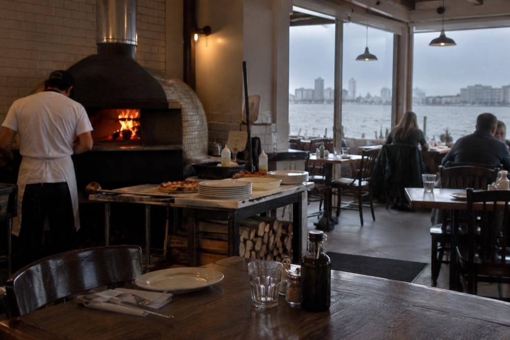 A neighborhood pizzeria dining room with a wood oven and simple tables