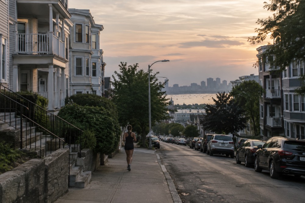 A quiet residential street of triple-decker houses on a hill at dusk