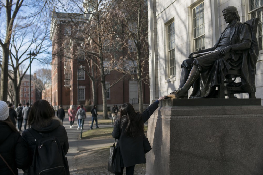 The John Harvard Statue with tourists rubbing its polished shoe