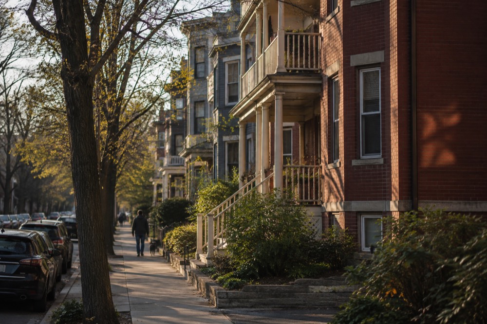 A red brick triple-decker house with a porch and steps to the sidewalk