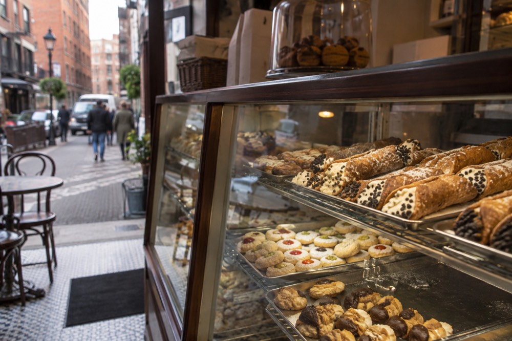 Pastry shop counter with trays of cannoli and Italian cookies behind glass
