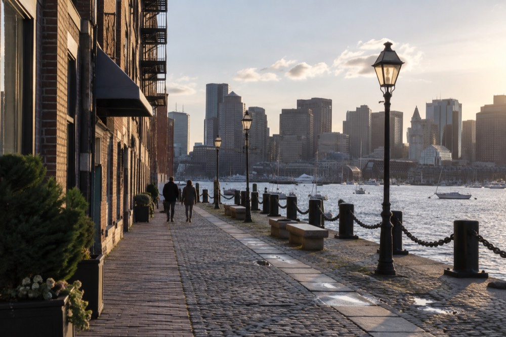 Waterfront walkway with harbor water, boats and city skyline in the background