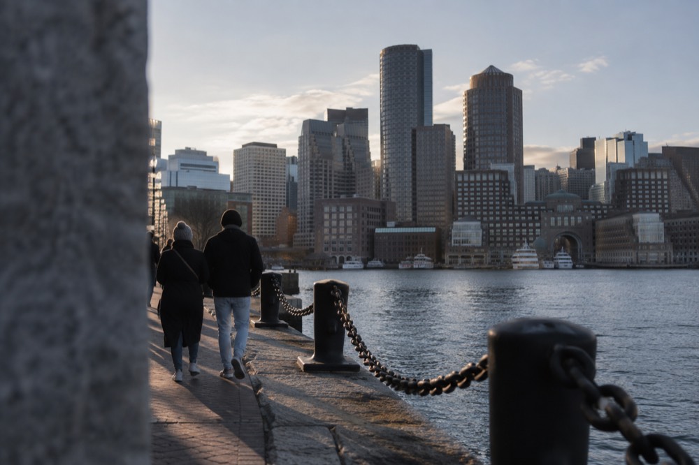 People walking the Harborwalk beside Boston Harbor with the downtown skyline across the water