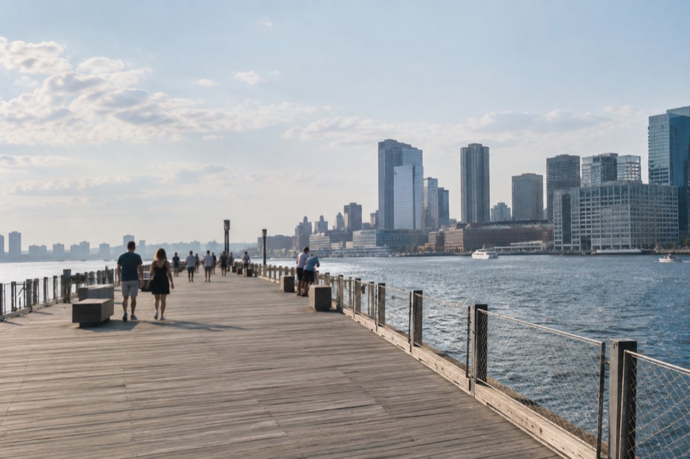 Visitors on a wide wooden pier extending into Boston Harbor near contemporary buildings