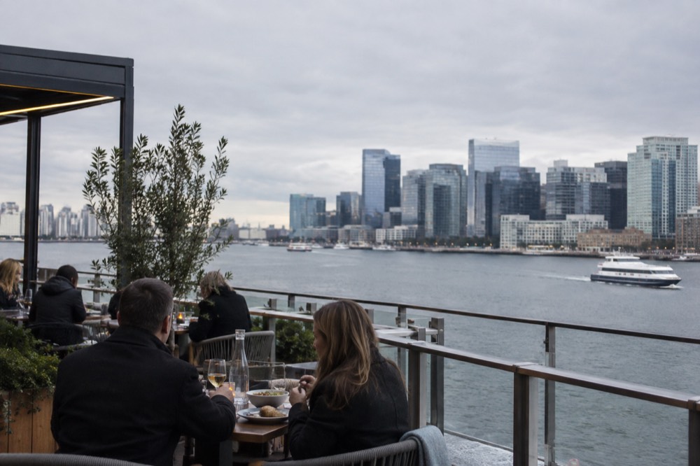 Diners at an outdoor waterfront restaurant table with harbor views in the Seaport District