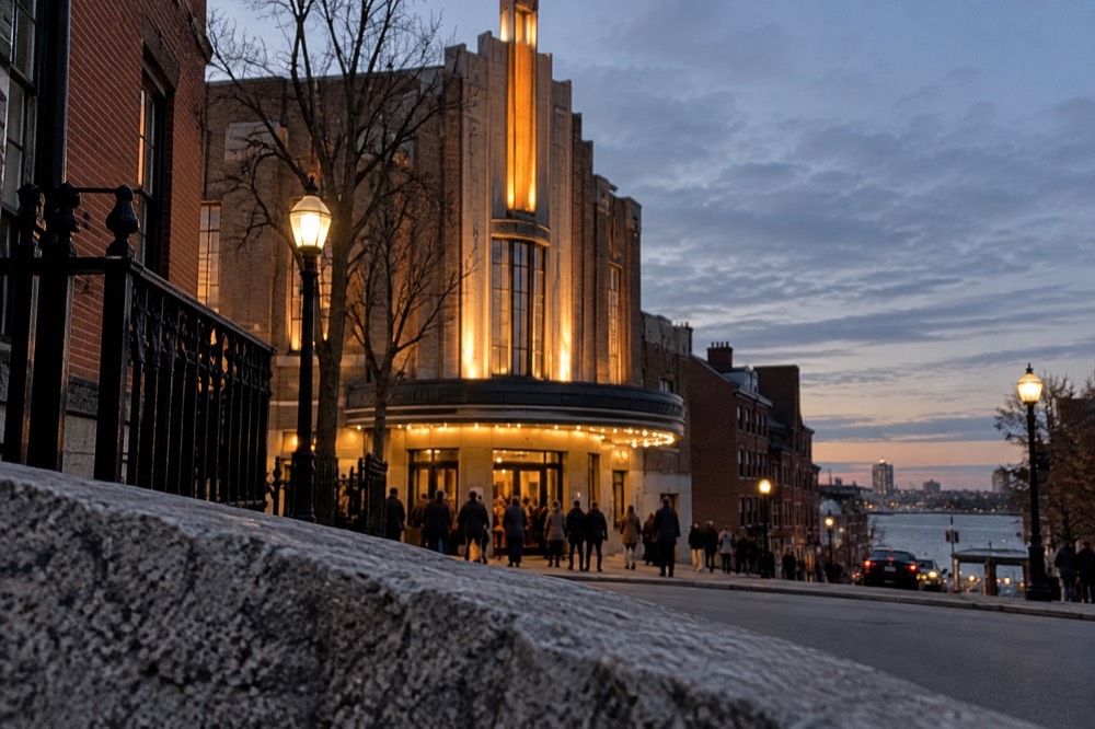 An art deco theater facade on a city square at dusk with a small crowd outside