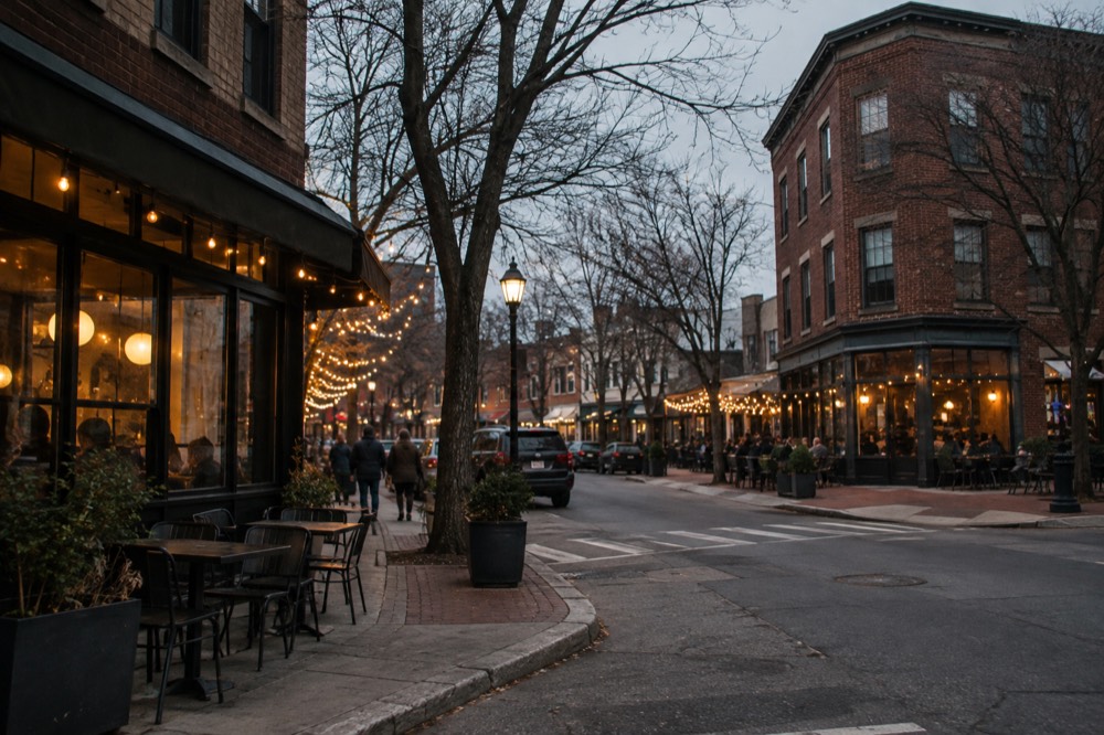 A corner intersection of brick low-rise buildings with restaurants and string lights in the evening