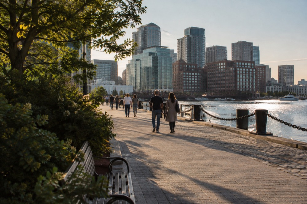 A riverside boardwalk with apartment towers, shops and people strolling at golden hour