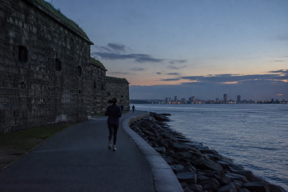 A granite fort with dark stone walls beside a bay with calm water and a walkway circling the shore