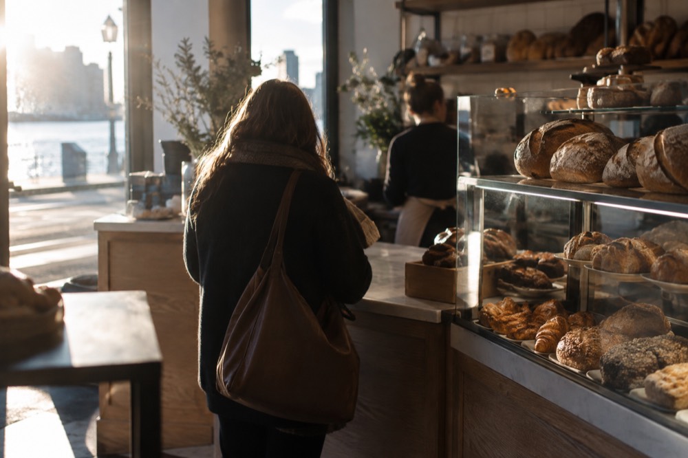 A small bakery counter with breads in glass cases and a customer ordering