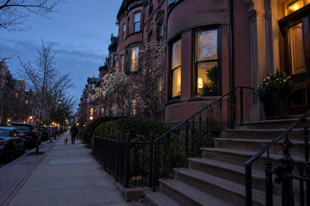 A brick rowhouse facade with a bowfront bay window and iron railing in evening light