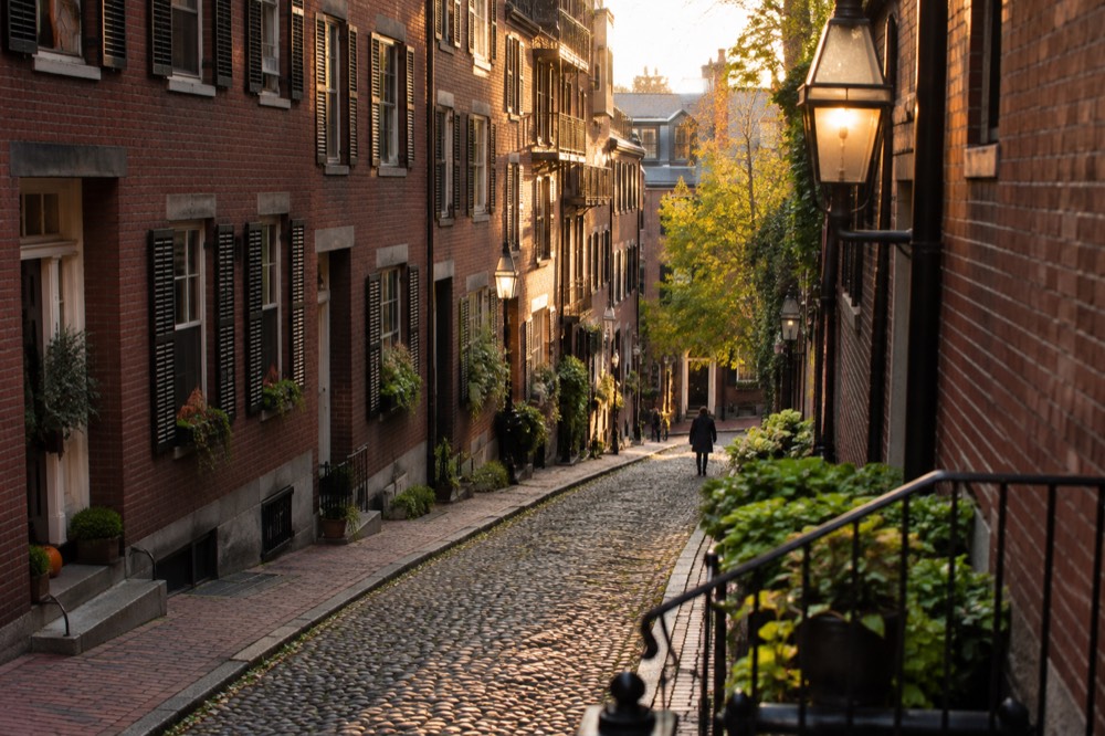 A red-brick Boston street with gas-style lamps and row houses in late afternoon light